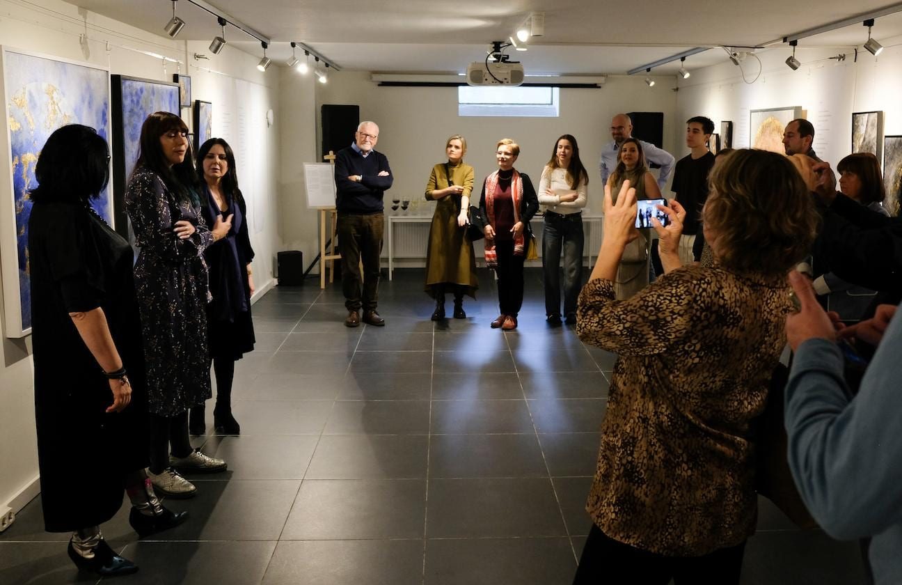 Visitors in the room during the opening, blue and gold planetary paintings along both walls and someone addressing the gathering.
