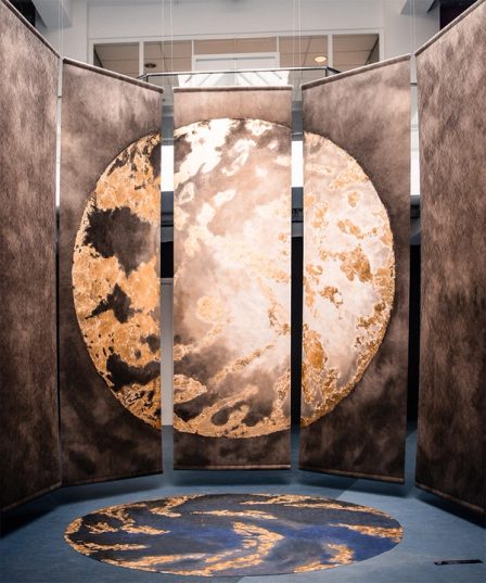 Five hanging panels in a half circle, together a moon in gold and grey, with a round disc of the same image on the floor.