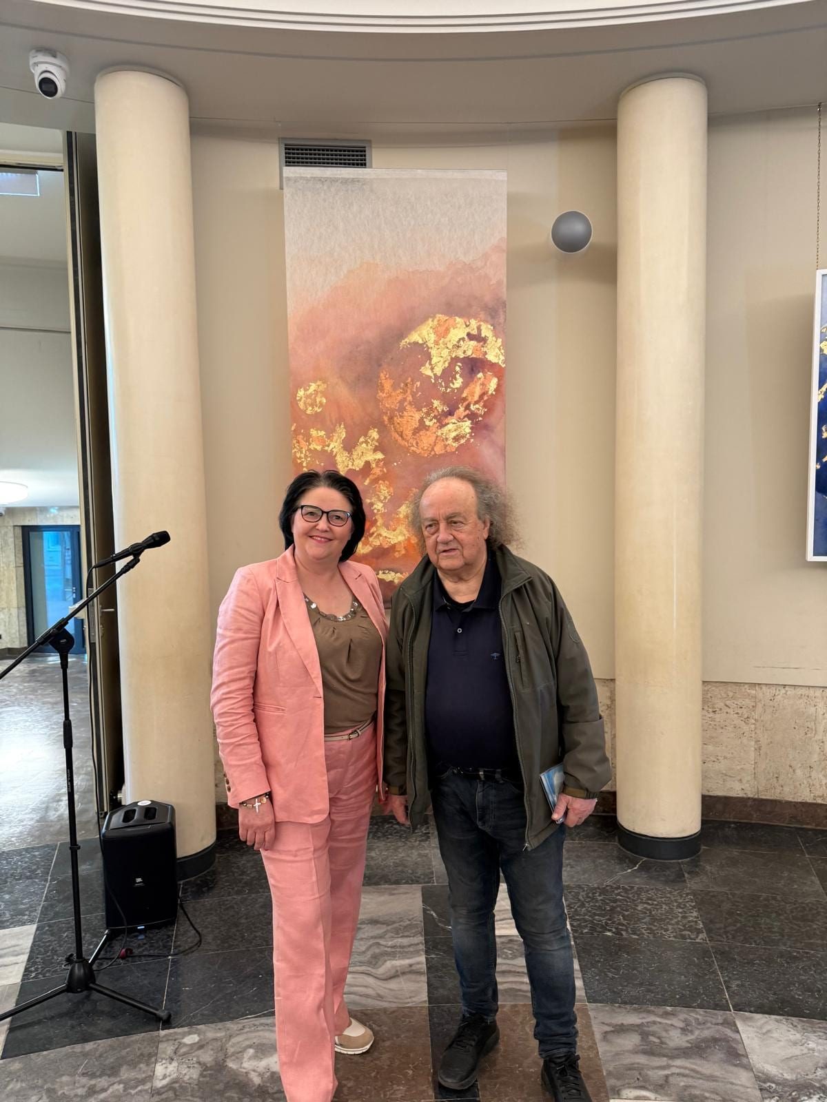 Two visitors with a programme in front of the coral work, between two columns of the foyer.