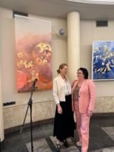 The artist in conversation with a visitor in the round travertine foyer, between the coral work and a blue and gold planet in a white frame.