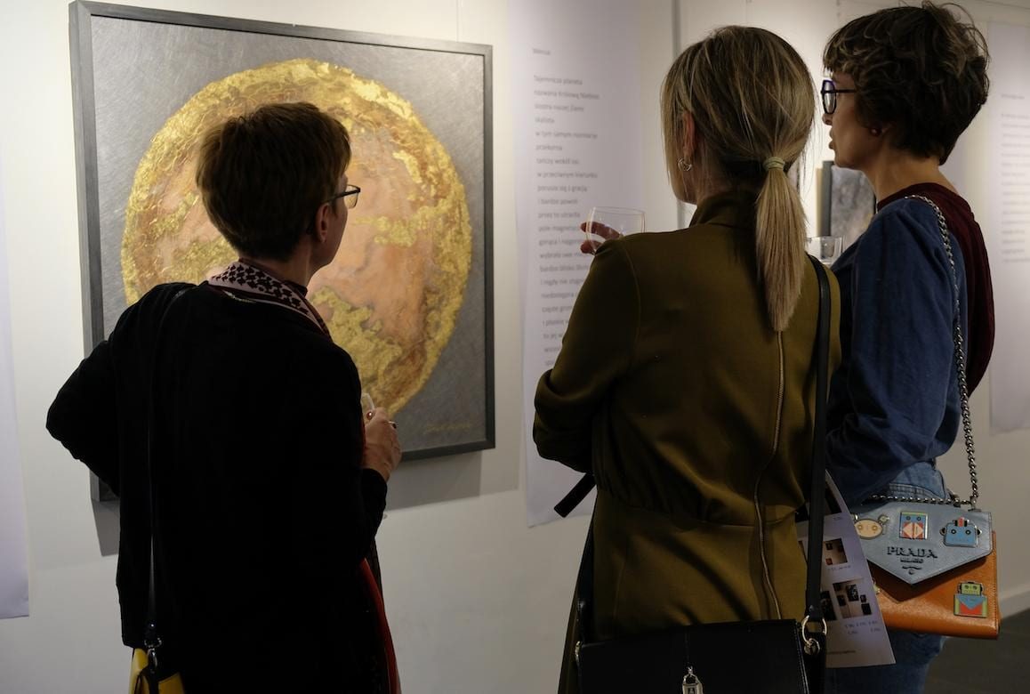 Three visitors in front of the peach planet, one of them reading the poem beside it.