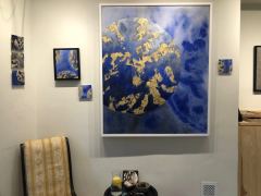 A large blue and gold planet in a white frame, with a series of small works beside it on the same wall.
