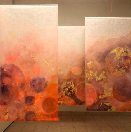 Three free-hanging panels in orange, pink and gold, planets emerging from the haze.