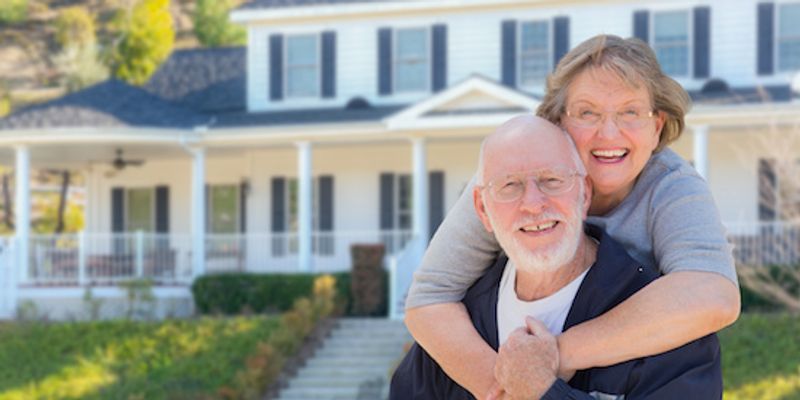 Senior couple standing in front of new house.