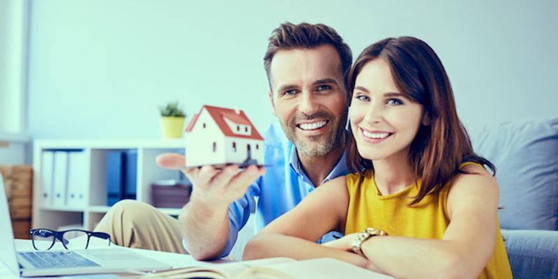 Couple holding house model and reading documents.