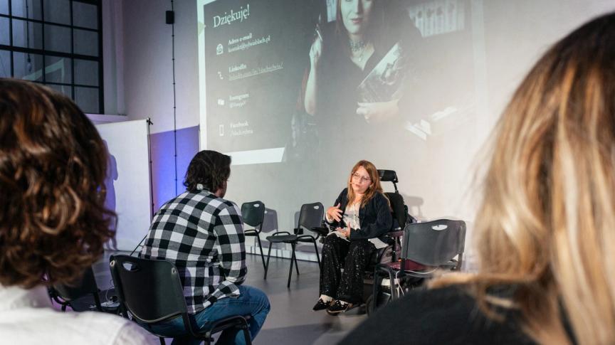 Sylwia Błach gives a lecture on art created by people with disabilities. She sits in a wheelchair in front of an audience and answers the questions.