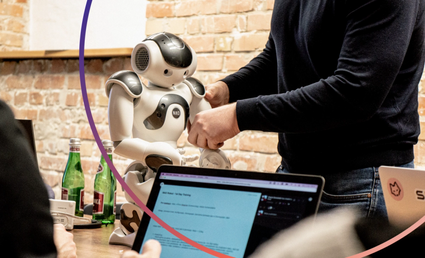 Robot - NAO sitting on a desk with a man holding his arm