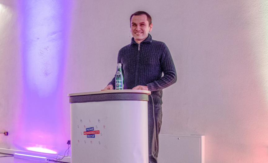 There is Przemek Kielar, a speaker at the Poznan Accessibility Meetup 3. He is standing by the rostrum.