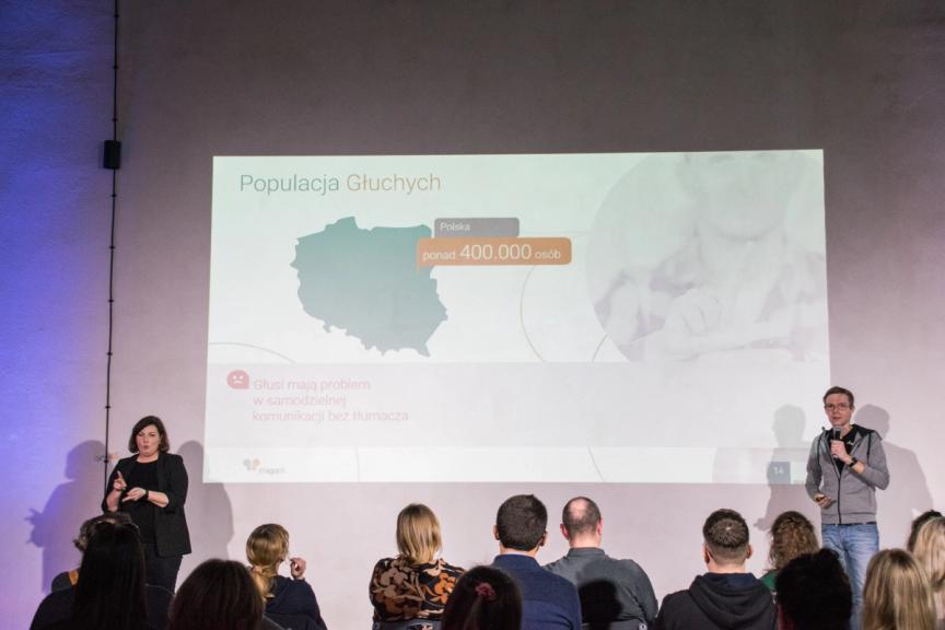 Paweł Potakowski standing and showing statistics - over 400 000 people deaf in Poland.