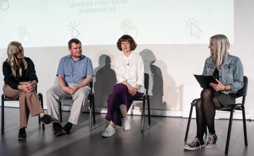 4 people sitting in chairs. 3 women and 1 man (2nd from left).