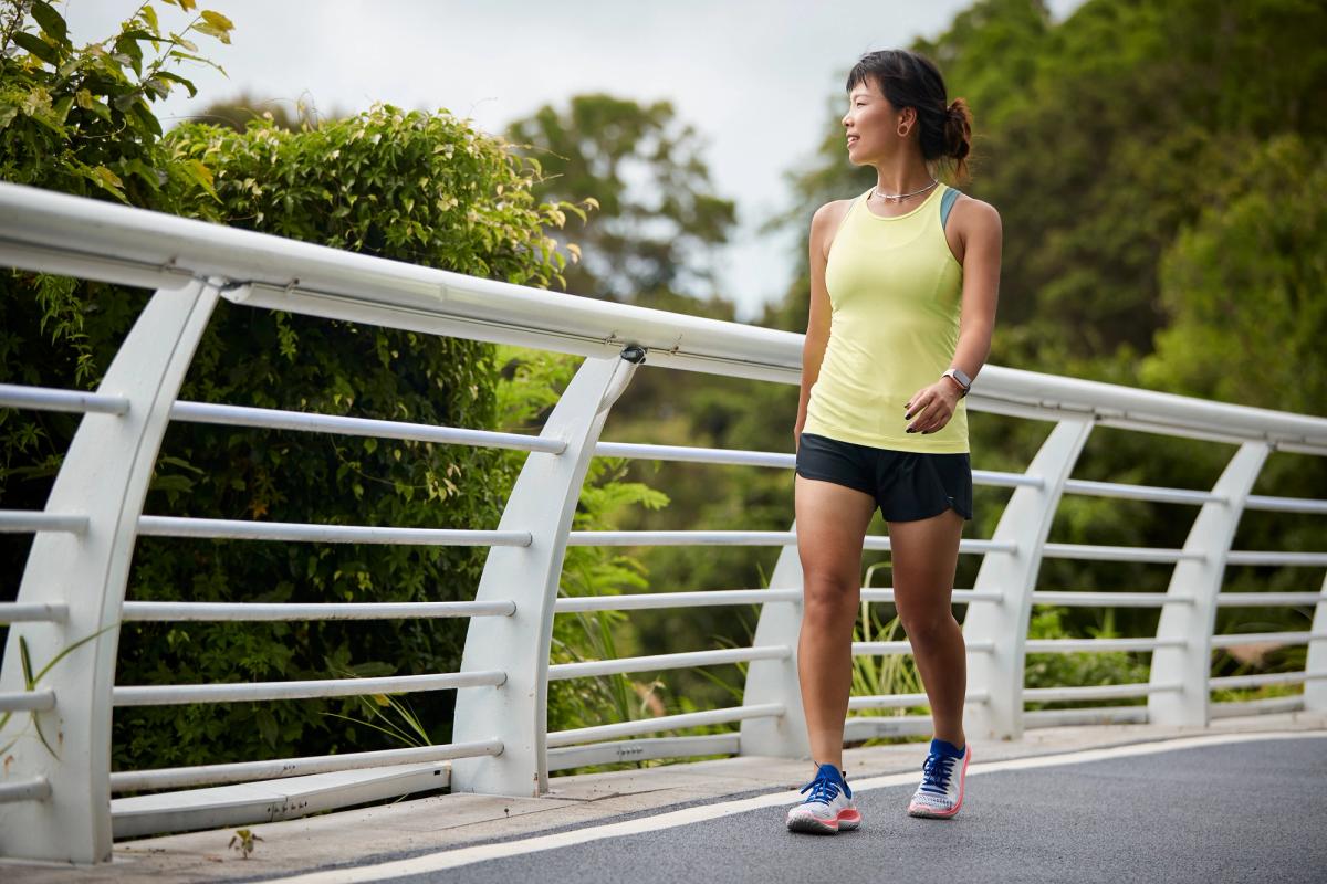 A woman walking across a bridge in a green park.