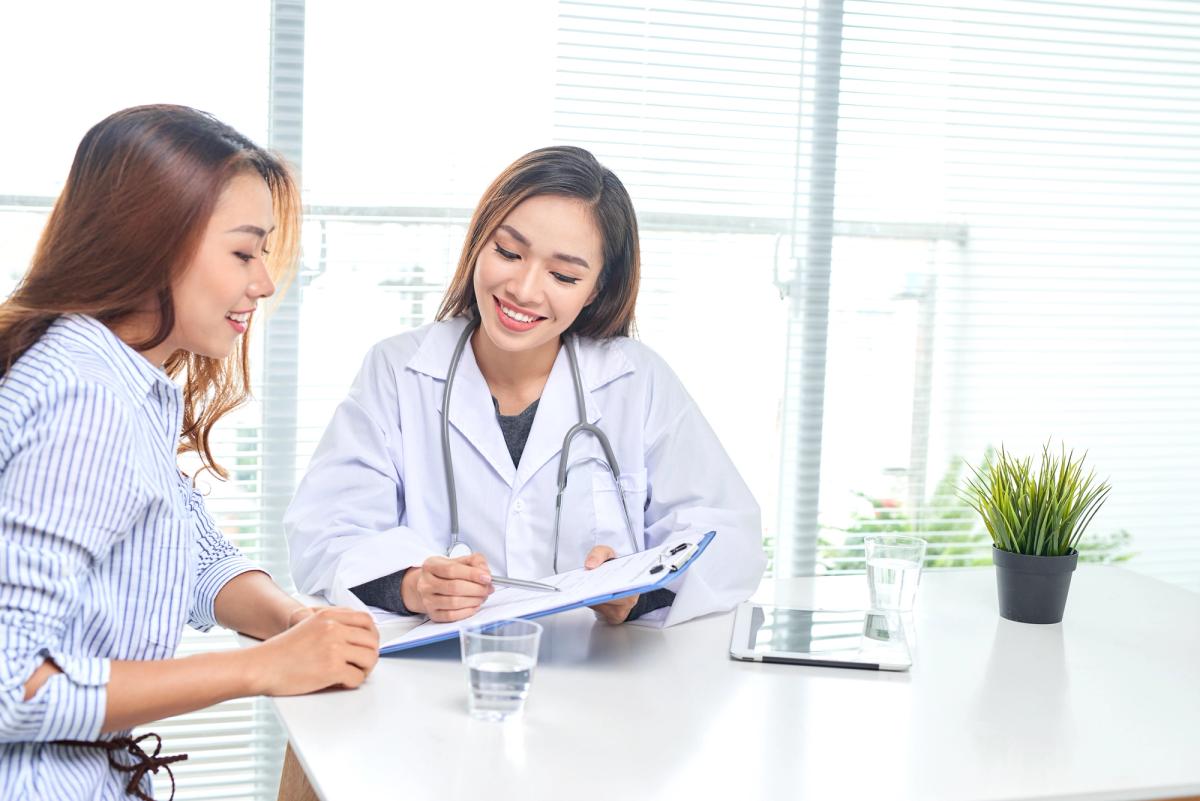 Two women talking across a desk, one wearing a white coat.