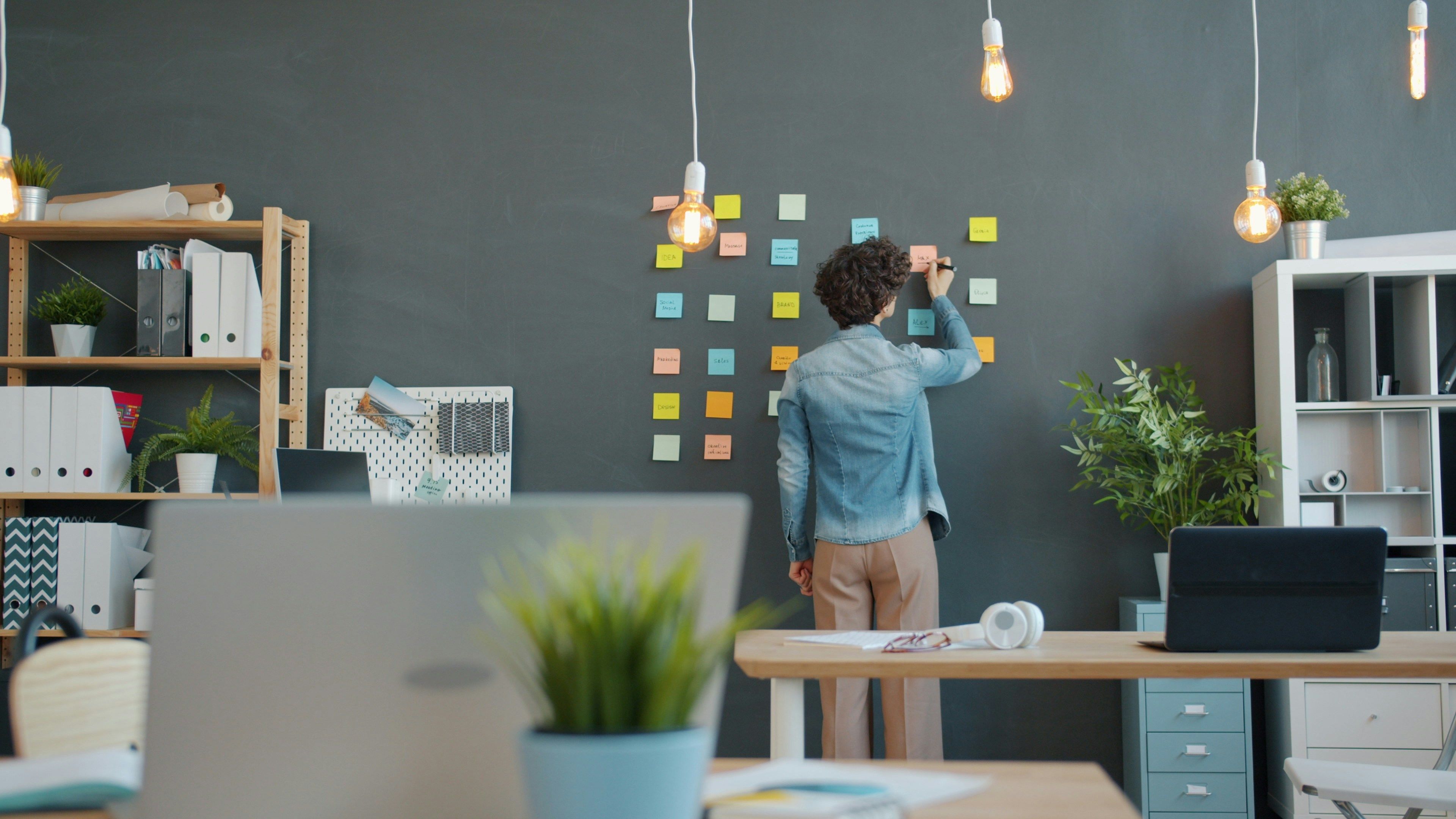 Person writing on colorful sticky notes in an office.