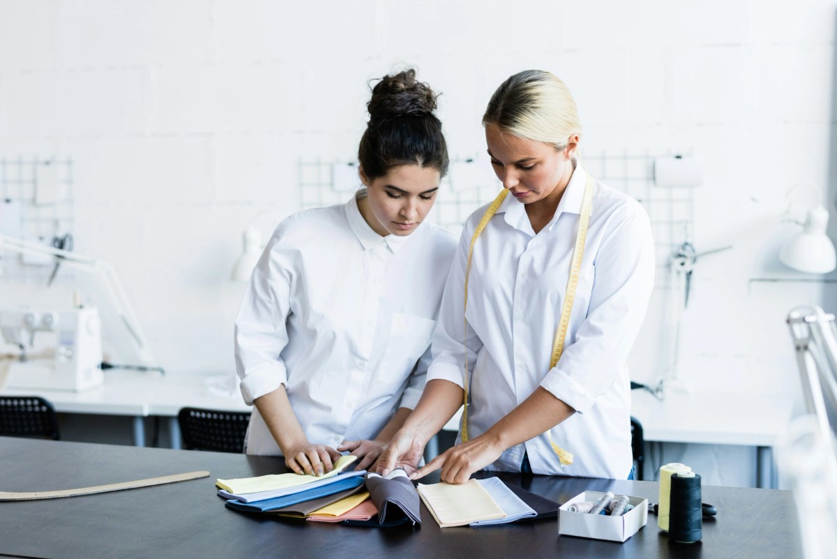 Шивачи и дизайнери работят върху дрехи в ателие – илюстрация за текстилната индустрия и въвеждането на Цифров продуктов паспорт.