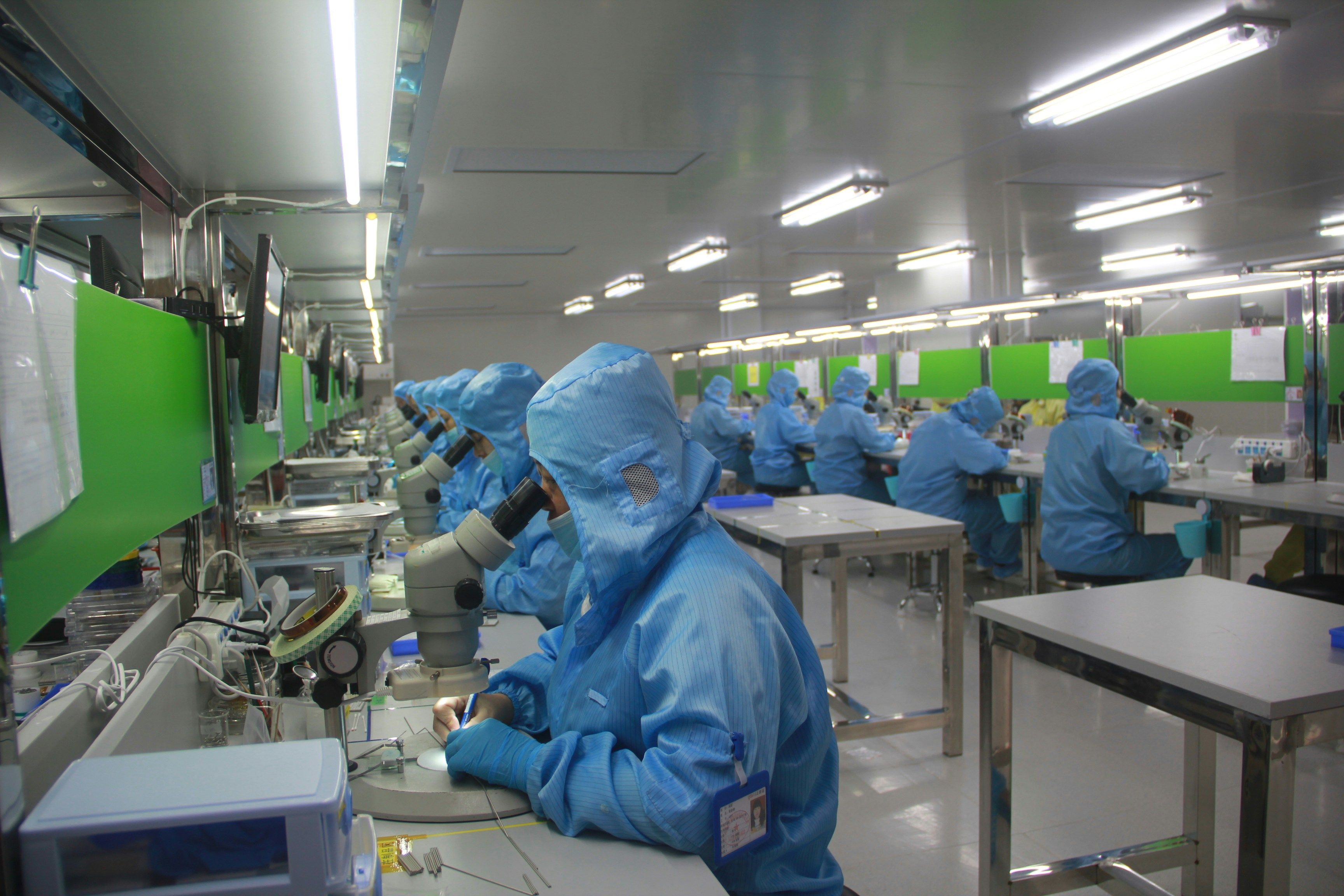 Muncitori dintr-o hală de electronică de precizie asamblează componente care ajung în produsul finit al altcuiva.