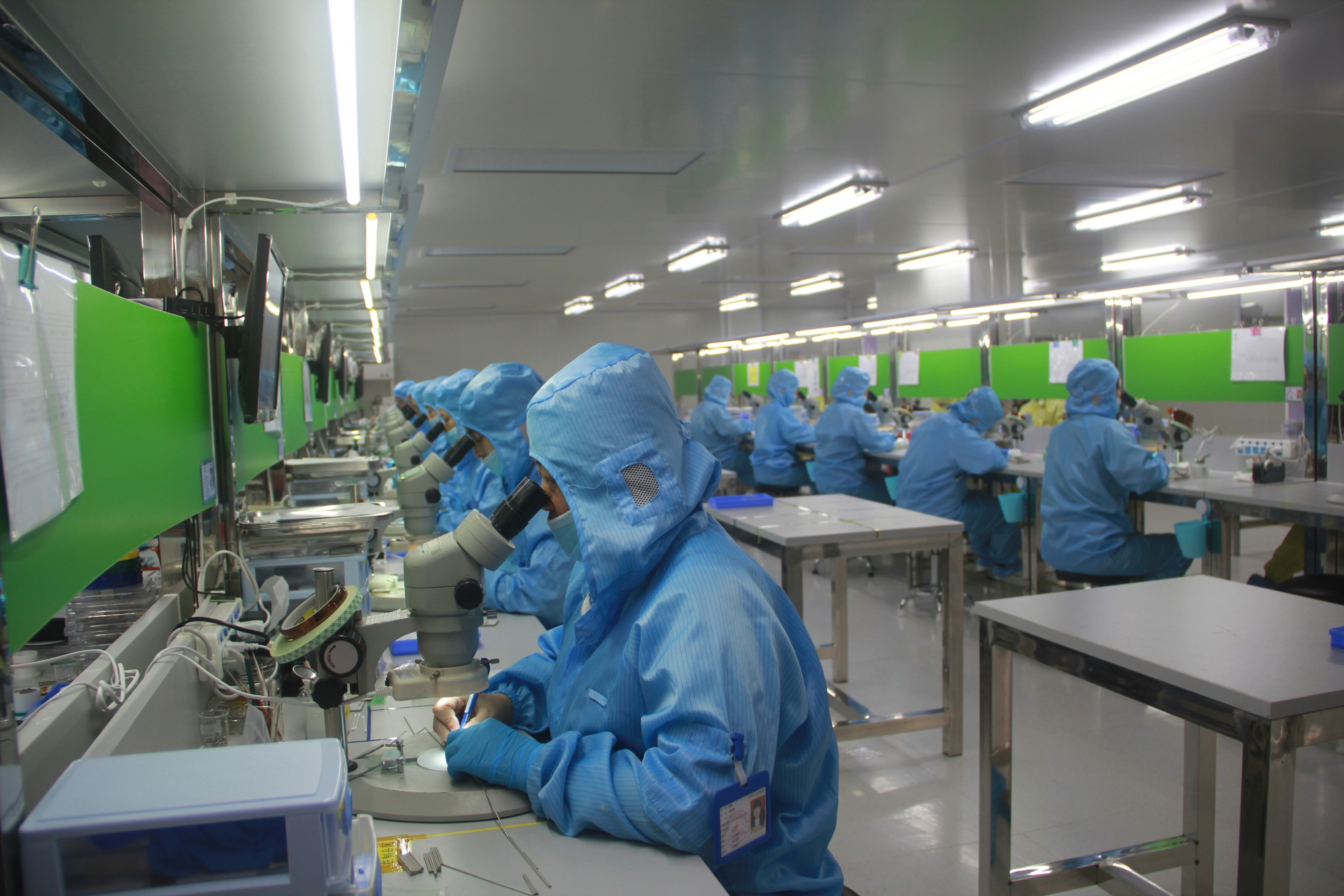 Muncitori dintr-o hală de electronică de precizie asamblează componente care ajung în produsul finit al altcuiva.