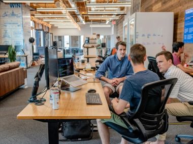 Three people talking in an open plan office about code.