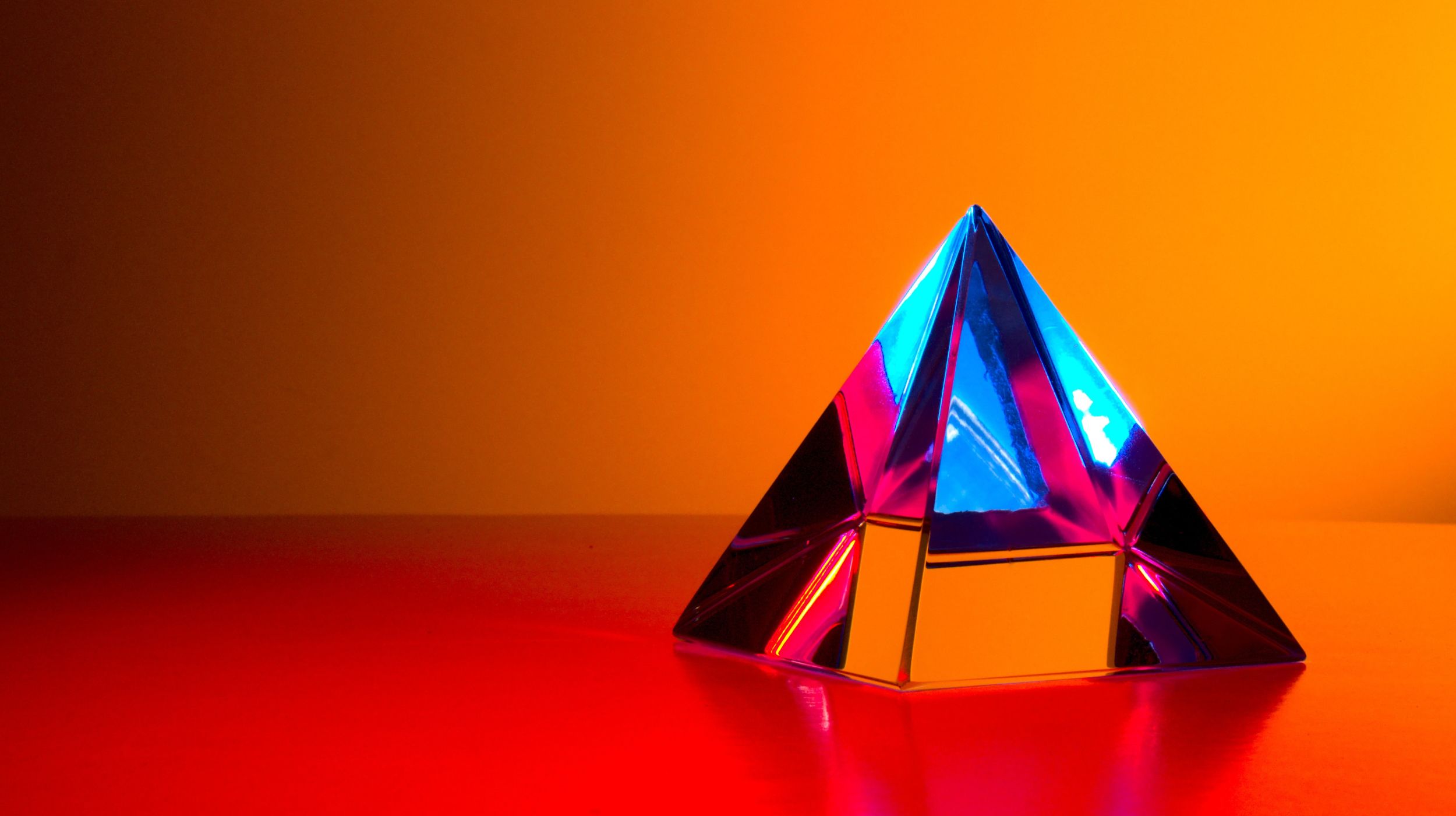 A glass pyramid on an orange table and background reflecting the blue sky