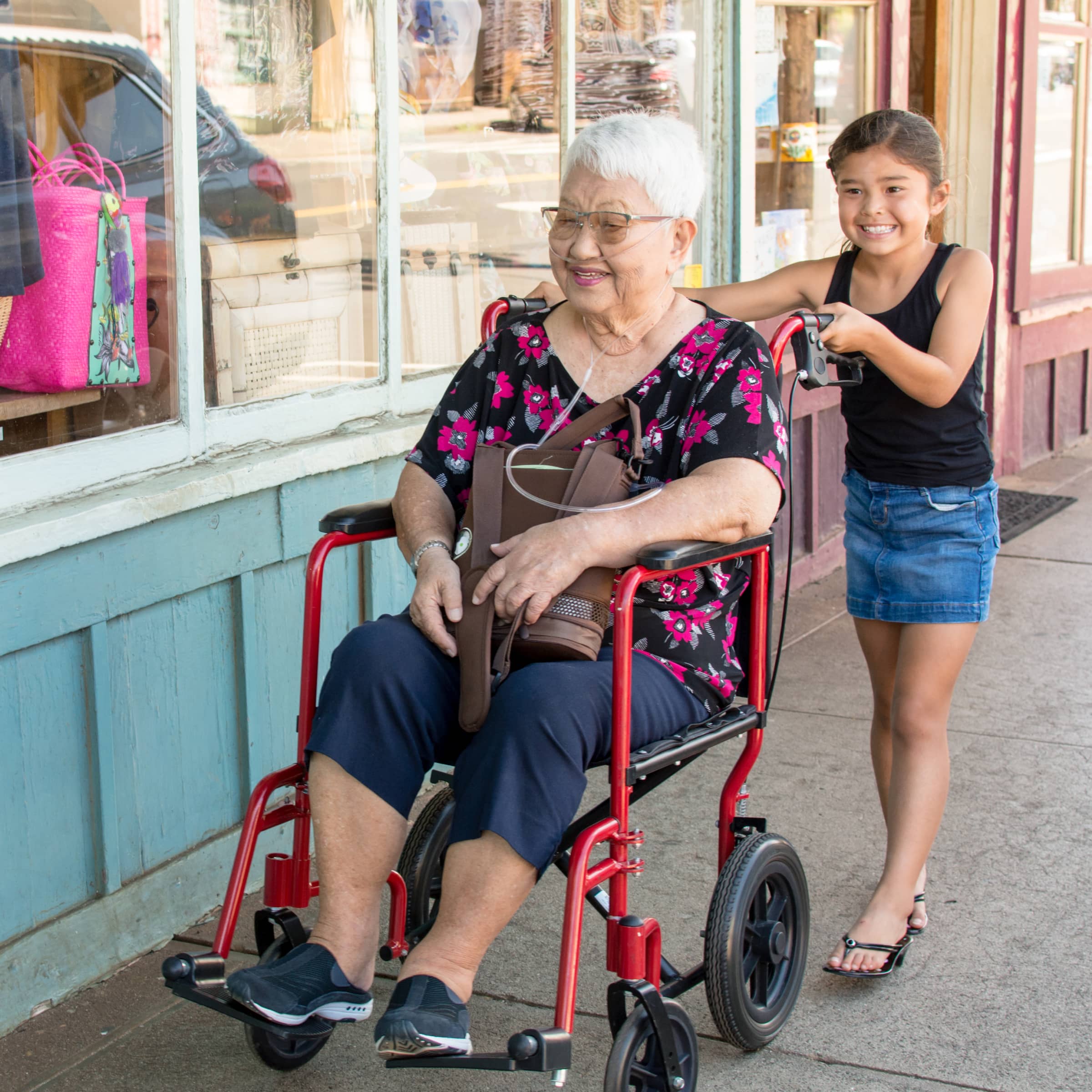 girl-assisting-elderly-woman-in-wheelchair-sidewalk