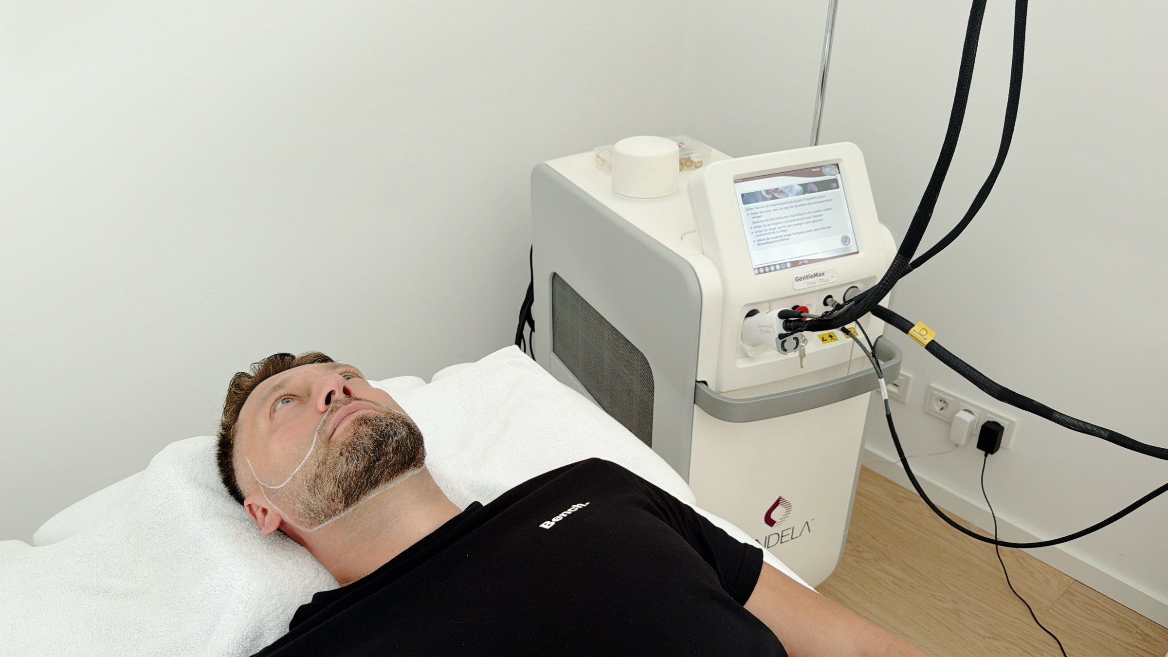 Ein Mann liegt auf der Behandlungsliege, neben ihm steht das Laser-Gerät mit Bildschirm.