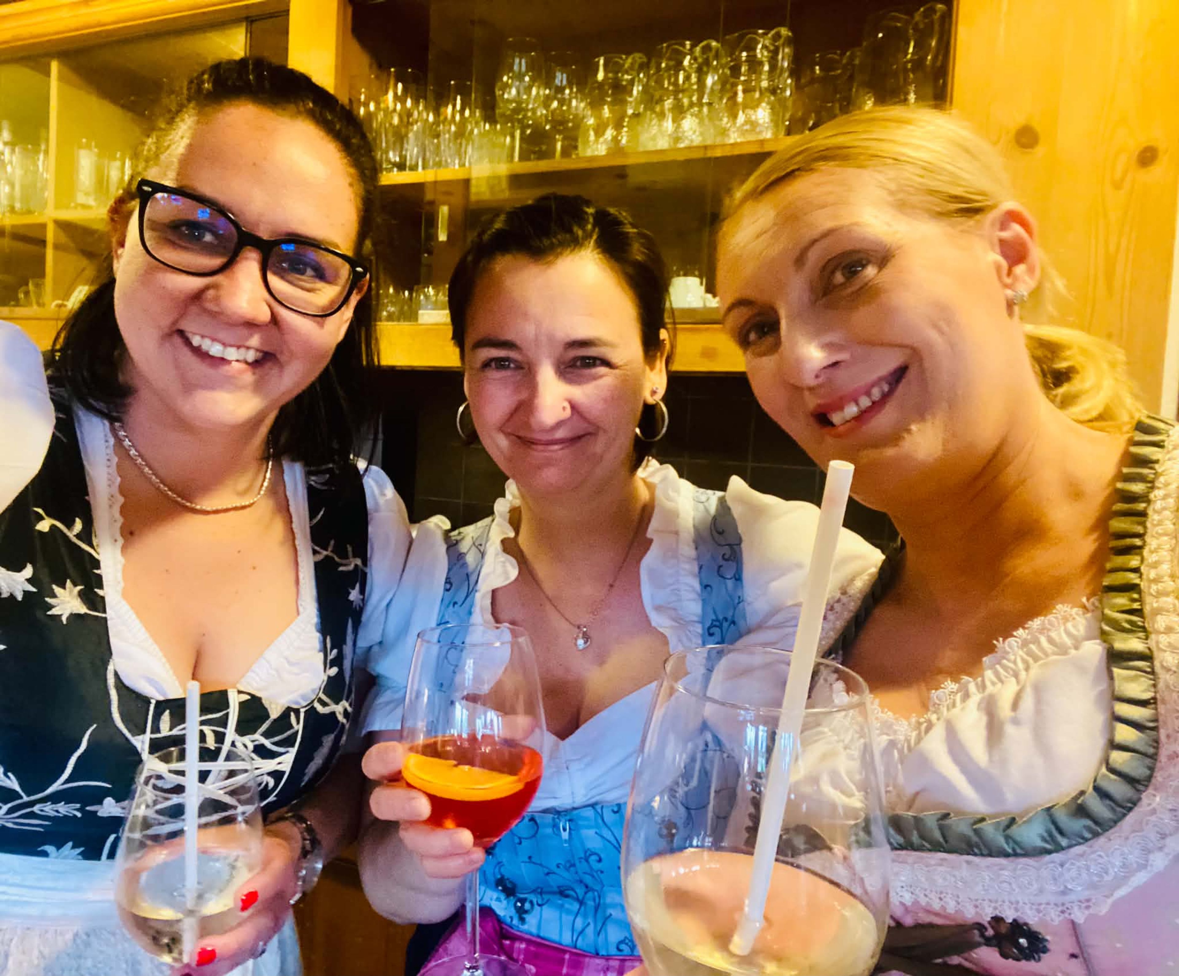 Drei Mitarbeiterinnen im Dirndl stoßen mit Getränken an