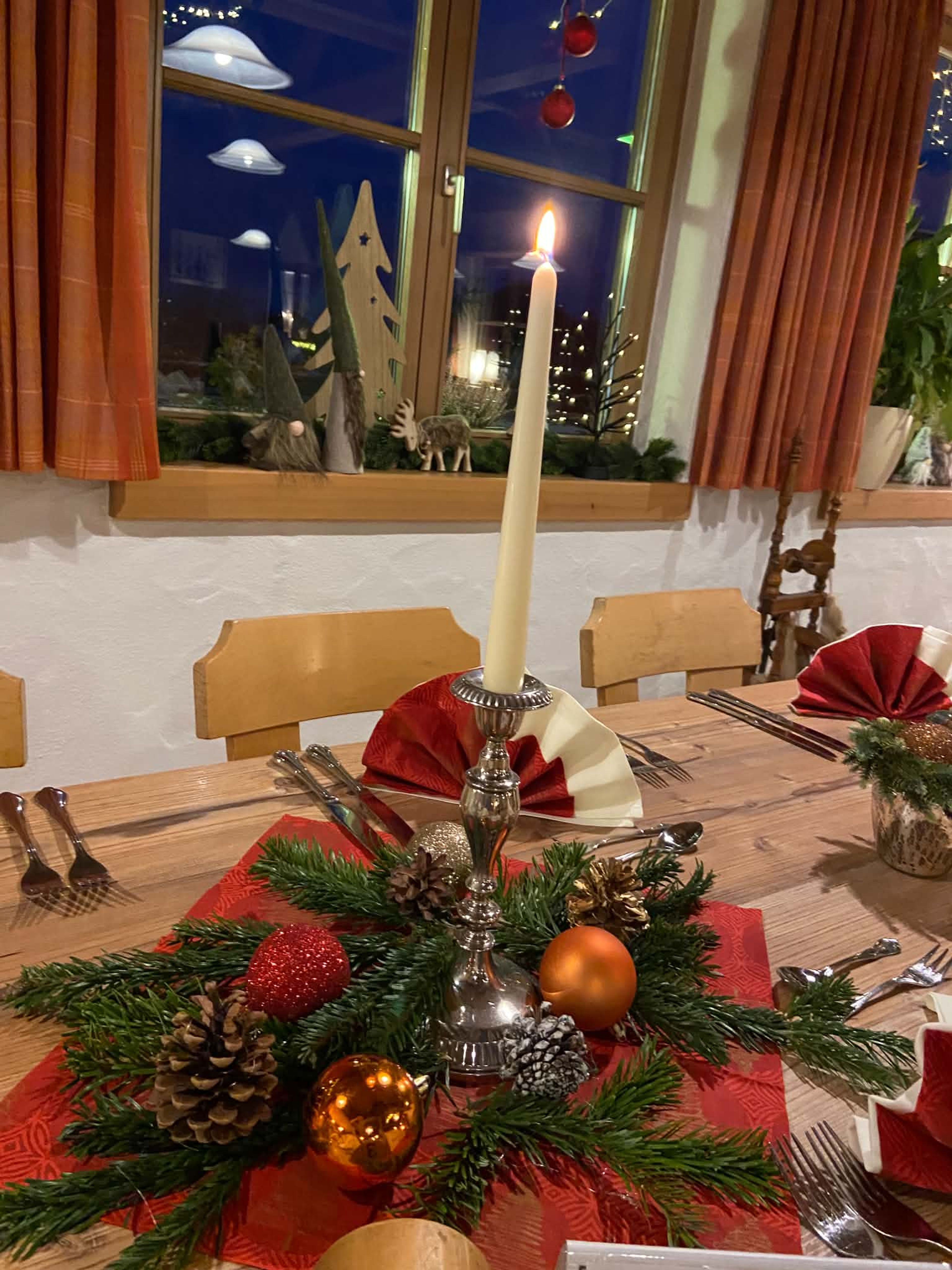 Tisch mit Kerze, Tannengrün und Christbaumkugeln, dahinter das weihnachtlich geschmückte Fenster