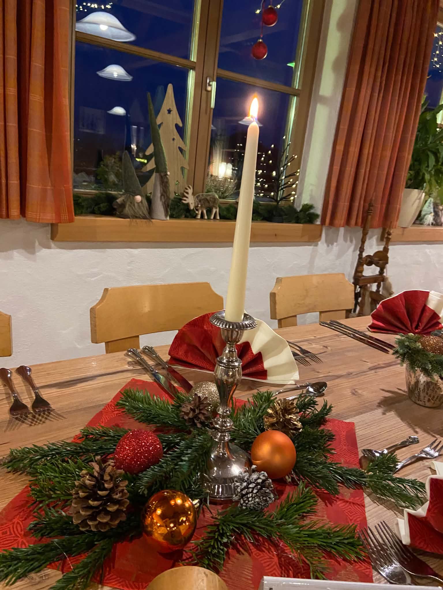 Tisch mit Kerze, Tannengrün und Christbaumkugeln, dahinter das weihnachtlich geschmückte Fenster