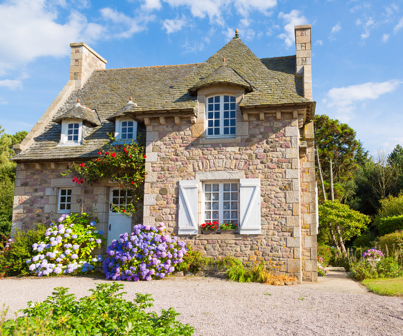 Photo of a French property showing the whole house. Various colourful flowers are in front of the property that are both pink, red and lavender.