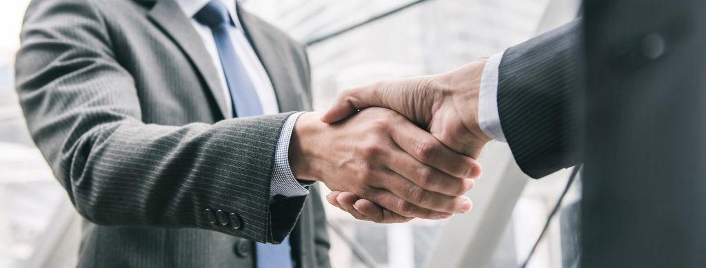 Close up of two people dressed in suits shaking hands.