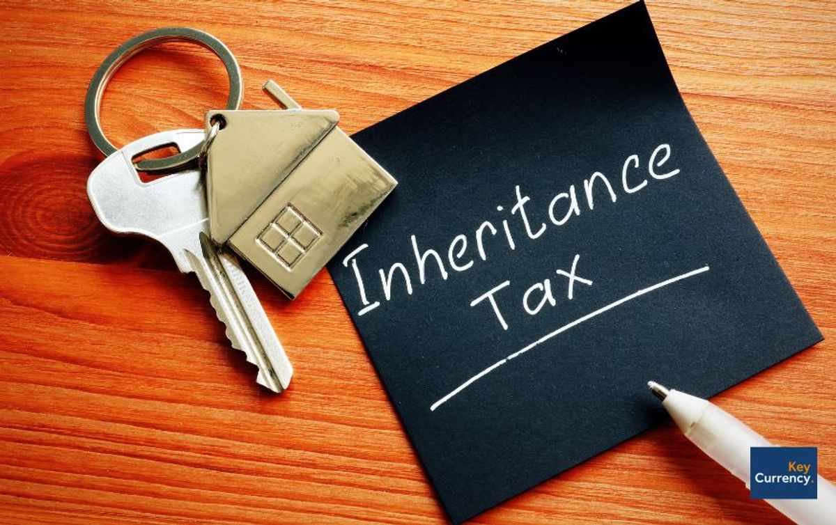 A black post-it note with 'inheritance tax' written on it. This note is placed next to a silver key with a house key ring attached to it. 