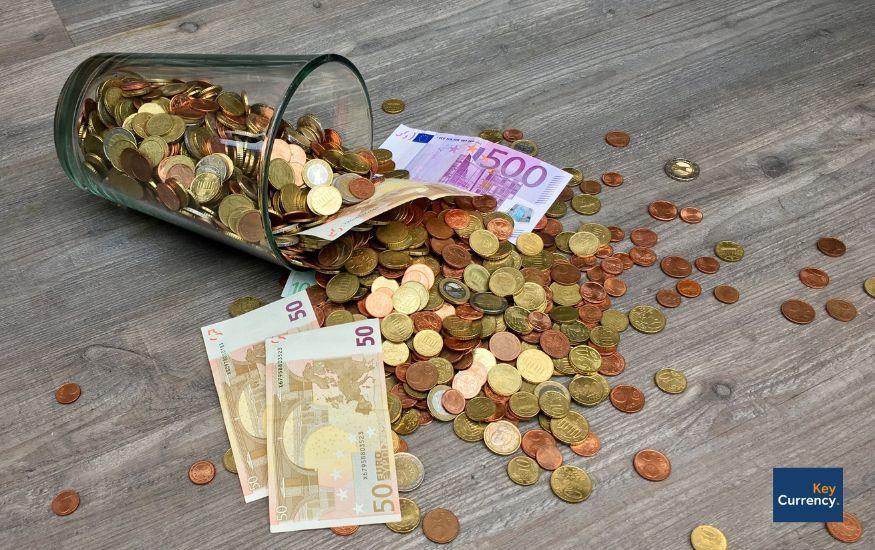 Euro coins and notes falling out of a glass on a wooden table.