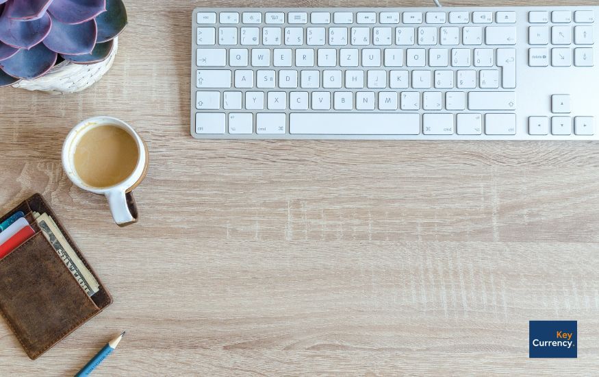 Overhead photo of an office desk including a keyboard, potted plant, cup of tea, wallet and a pen.