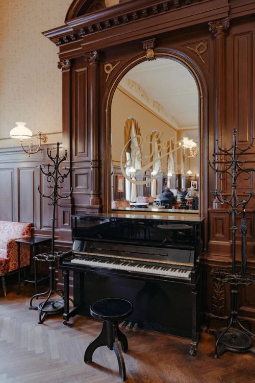 Schwarzes Klavier vor dem Spiegel mit dem Schriftzug „Café Sperl seit 1880“, daneben zwei Garderobenständer