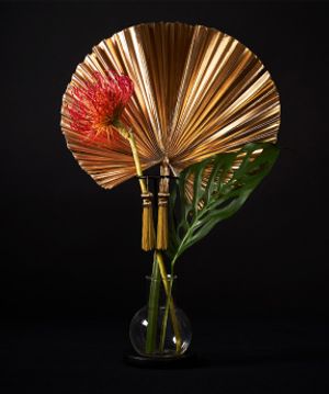 A gold fan, a red flower, and a large leaf in a vase