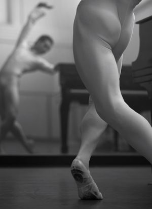 A ballerina dancing in front of a mirror with a grand piano