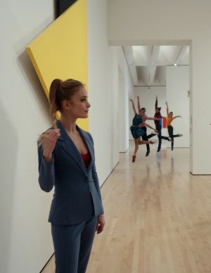 A woman looking at art in a gallery with a group of dancers behind her