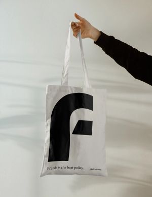 A hand holding up a tote bag with the Frank logo on it