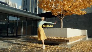 A dancer in a yellow skirt in an urban courtyard with fall leaves, overlayed with the text "SFMOMA"