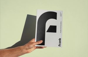 A hand holding a booklet with the Frank logo on it in front of a light green background