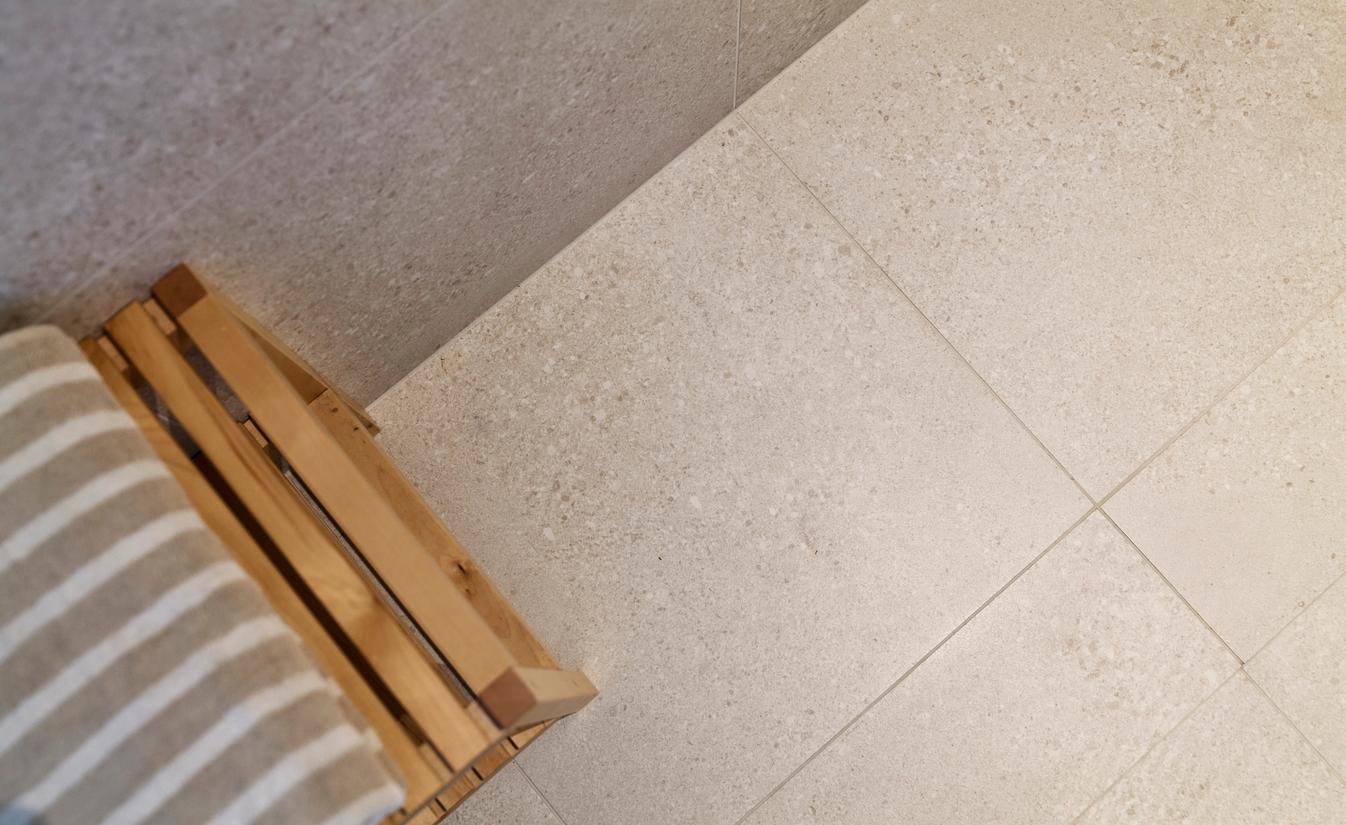 Baderomsgulv med store, beige fliser som gir et naturlig og rolig uttrykk. Utført av Lomundal.