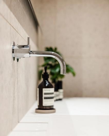 Detaljbilde av lyst og moderne baderom med innebygde armaturer over vask i krom. Badet er pusset opp av Lomundal.