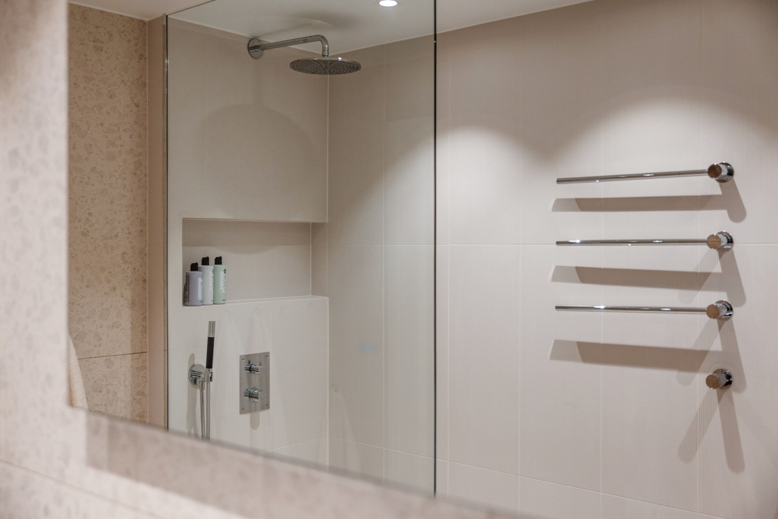 Detaljbilde av lyst bad med store beige fliser på vegg, innebygde armaturer i dusj med egen hyllenisje. Badet er pusset opp av Lomundal.