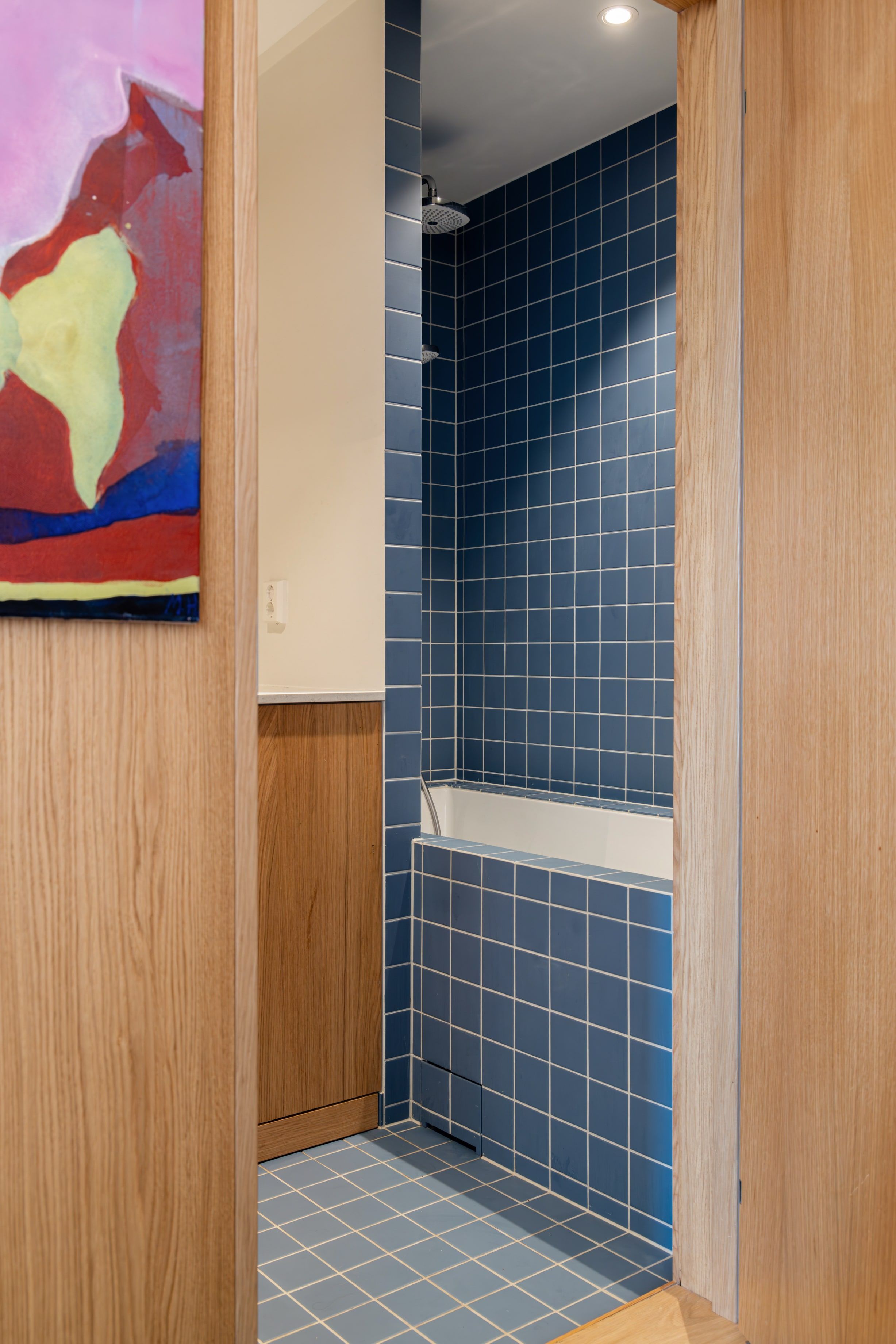 Innebygd badekar med blå kvadratiske fliser rundt badekar og på vegg. Badet er totalrenovert av Lomundal.