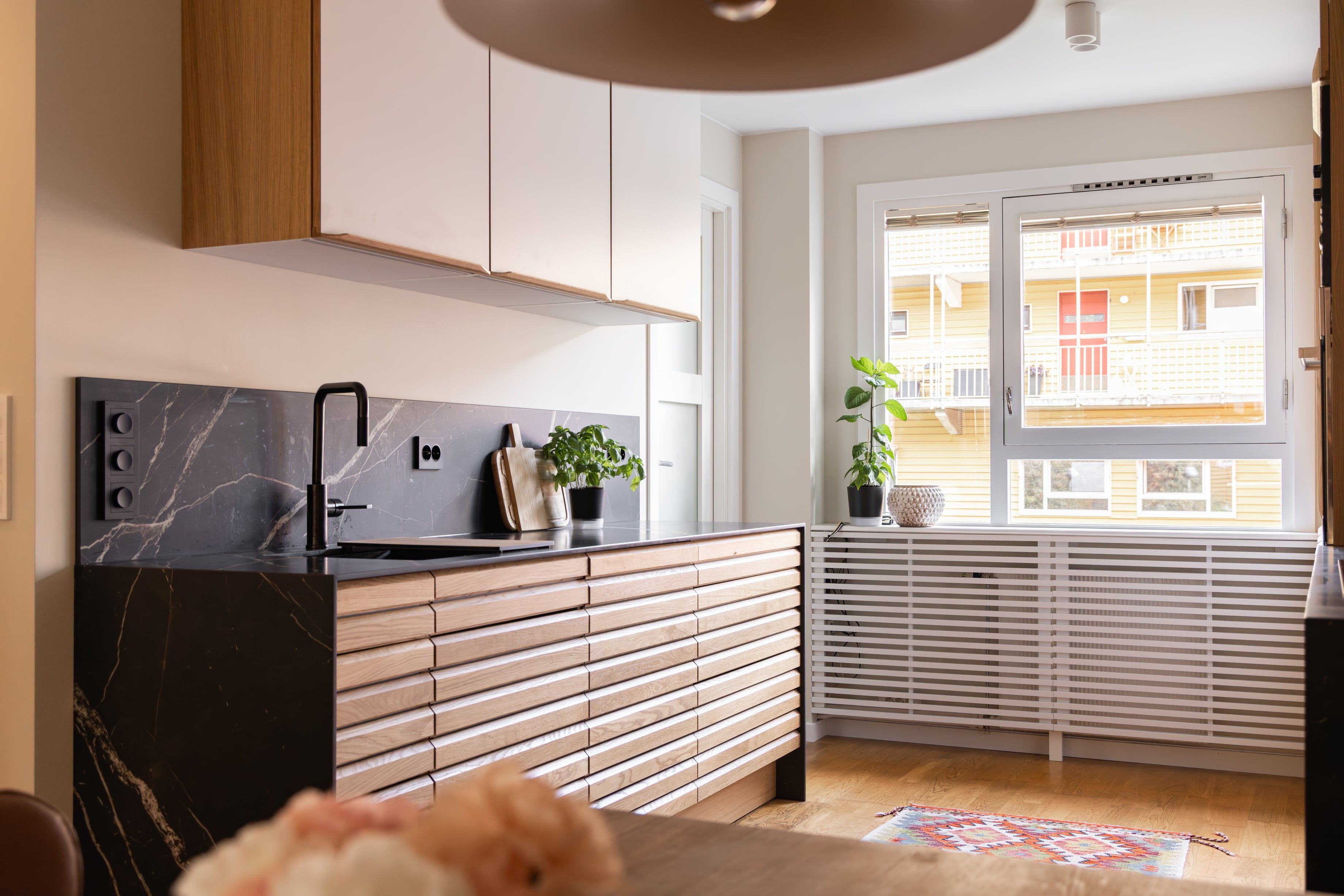 Kjøkken i nordisk stil med kjøkkenøy i lyst tre og benkeplate i mørk stein. Utført av Lomundal.