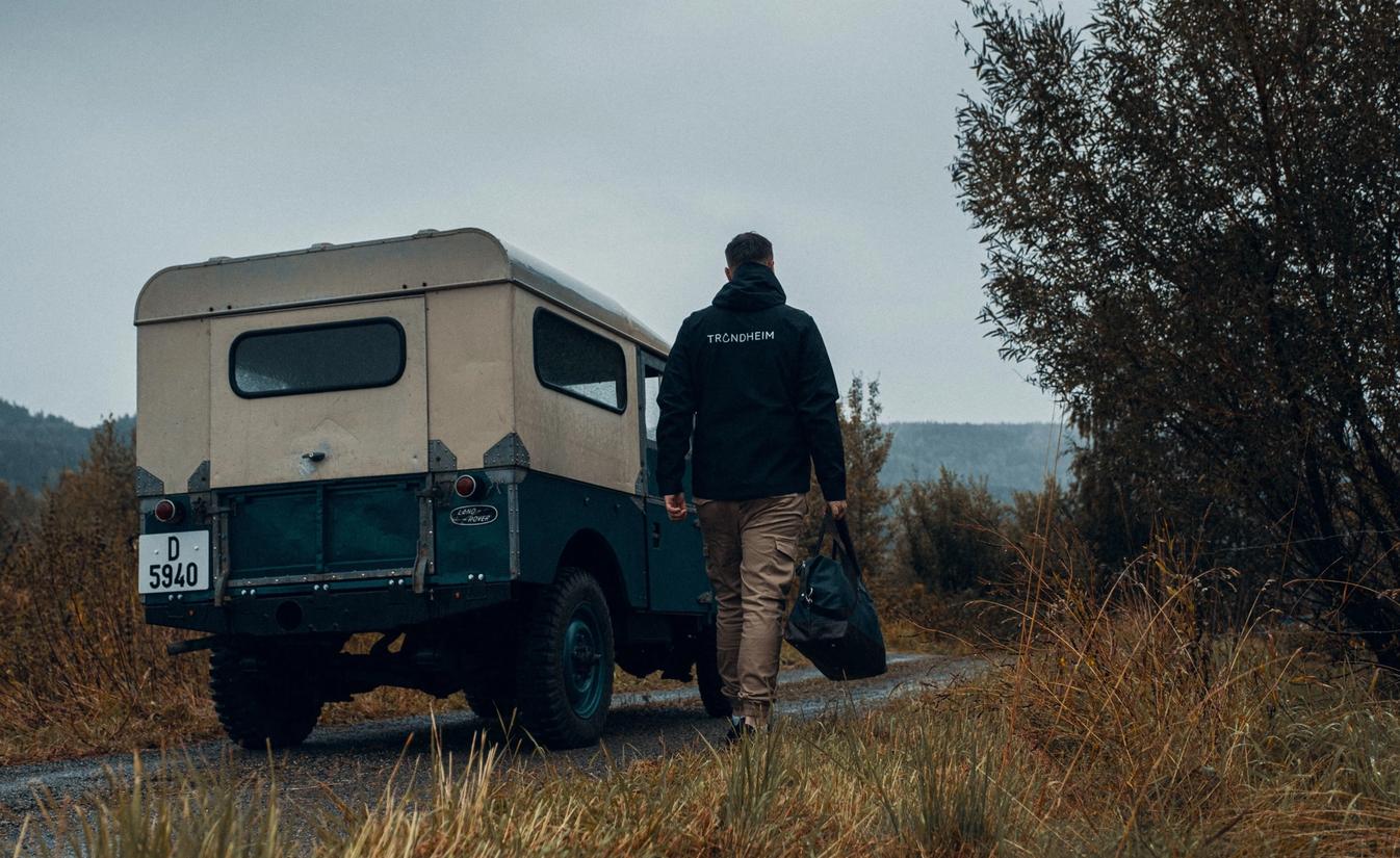 Bjørnar Lomundal holder en bag og går ved siden av veteranbilen sin.