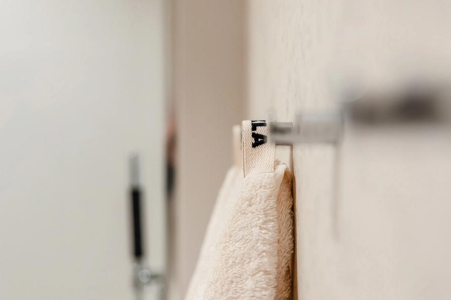 Detaljer på lyst og moderne bad med store lyse fliser på vegg. Vegghengte knagger til håndklær fra Tekla. Badet er pusset opp av Lomundal.