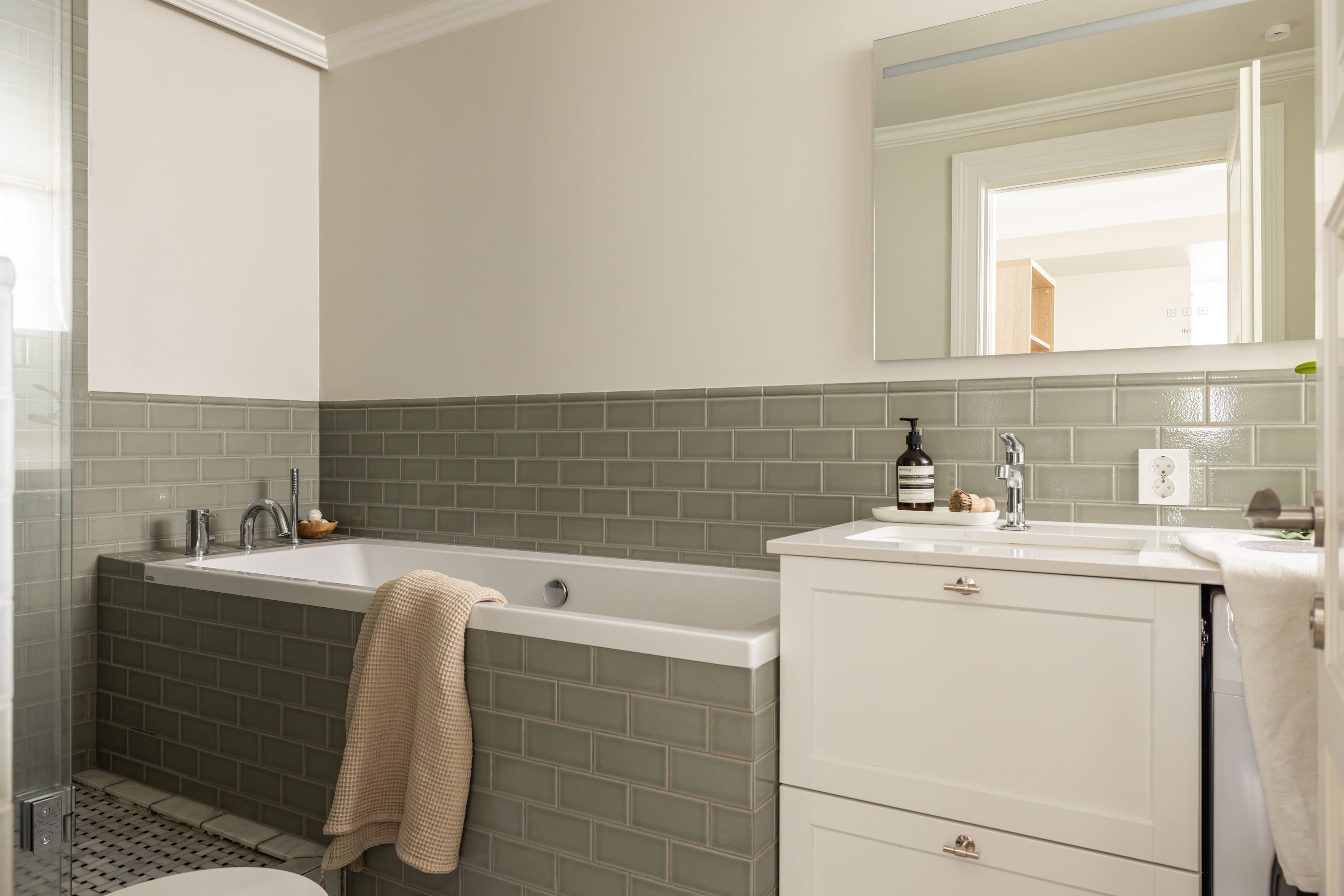 Klassisk bad med veggfliser i en dus grønntone. Badet har et tidløst uttrykk med en elegant kombinasjon av materialer og mønstre. Utført av Lomundal.