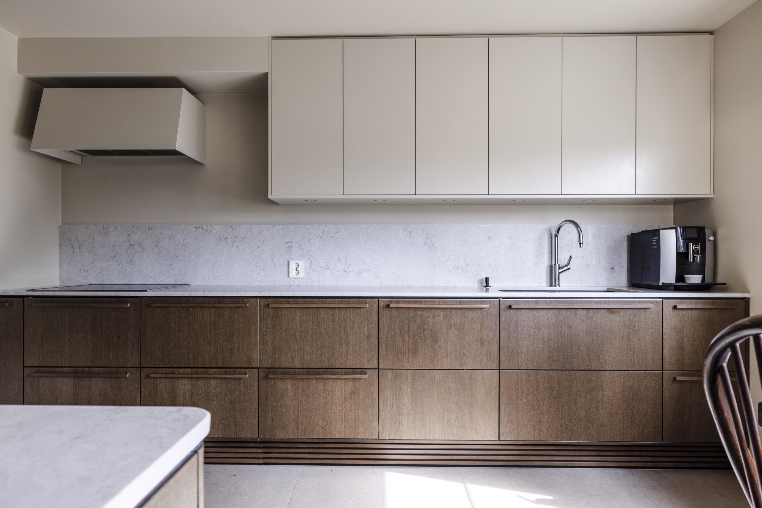Kjøkkeninnredning i valnøtt fra Sigdal med overskap malt i samme beige tone som veggen. Benkeplate i lys sten. Pusset opp av Lomundal.