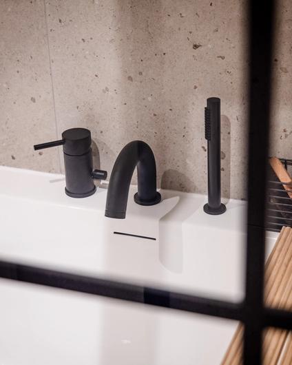 Detaljbilde av armaturer til badekar i sort matt. Flisene over er i en varm beige tone. Badet er pusset opp av Lomundal.