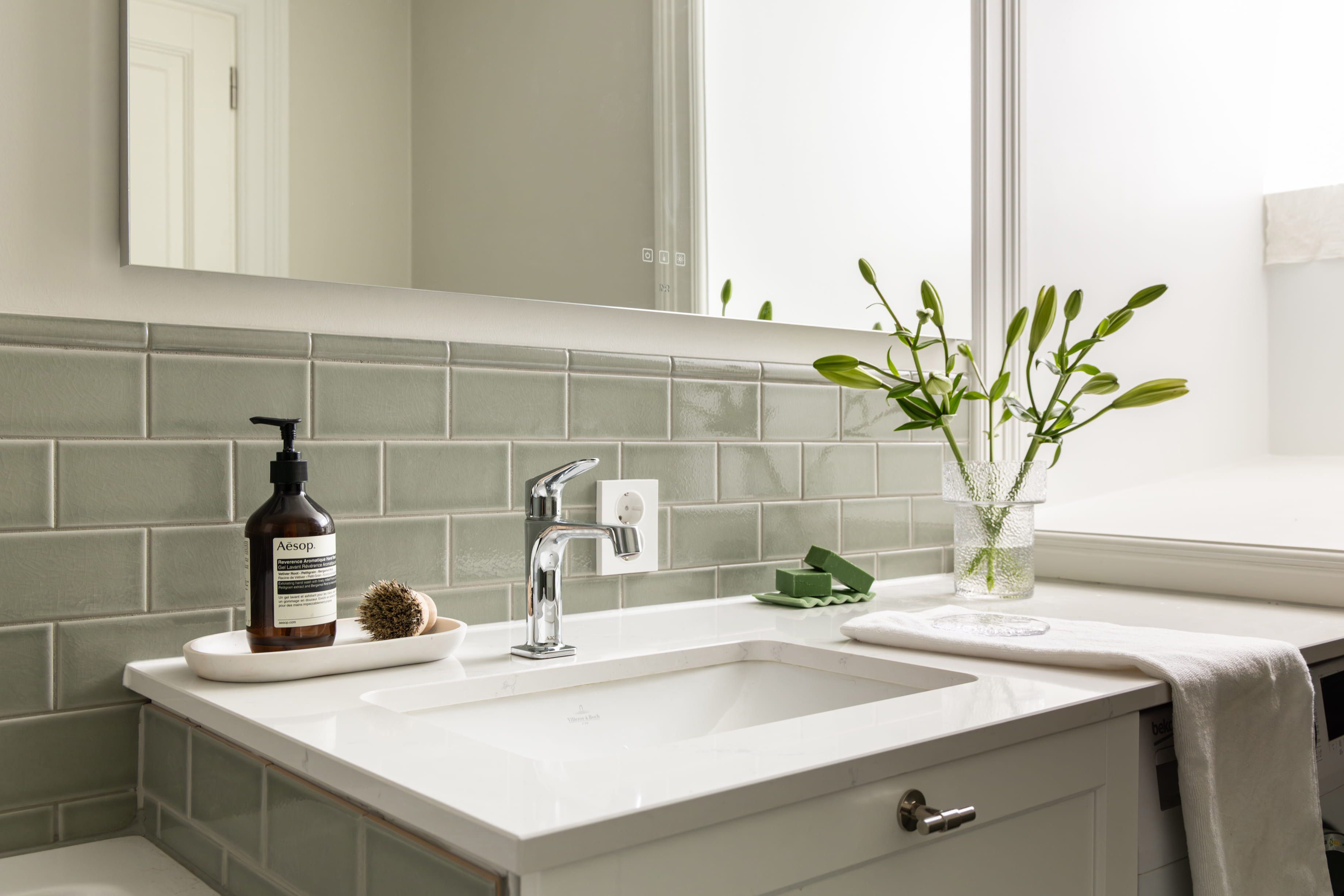 Et klassisk bad med hvit servant og grønne, blanke fliser på vegg i brystningshøyde. Utført av Lomundal.